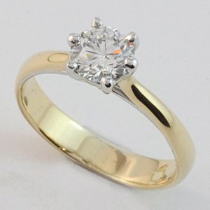 Six claw solitaire with the claws oriented across the finger on a 'soft' hammered band in 18 carat yellow and white gold.